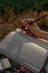 pexels-photo-8180719-8180719 Close-up of a woman writing in a journal outdoors on a sunny day.